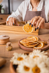 partial view of african american woman holding dried orange slice near camomiles on blurred foreground.