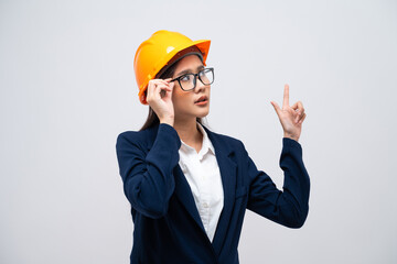 Portrait of Asian female engineer with hard hat pointing at copy space isolated on grey background.