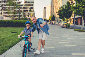 Photo of a young boy and his father on a bicycle lane, learning to ride a bike.
