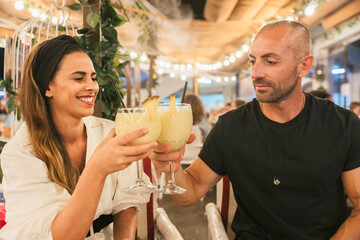 Young man and woman toasting with cocktail glasses in a restaurant at night. Nice couple during a romantic date