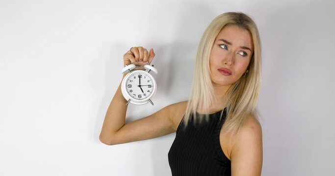 An attractive blonde haired woman holding up an old style alarm clock that is set to 5 o'clock, waking up at 5am or 5pm concept, filmed in 4k footage