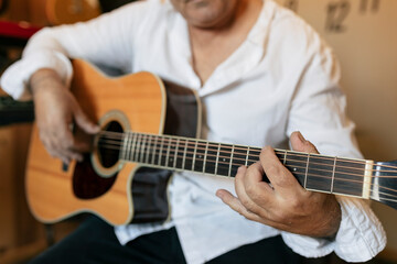 Obraz premium Crop anonymous middle aged male guitarist in white shirt performing song on acoustic guitar during rehearsal in daylight