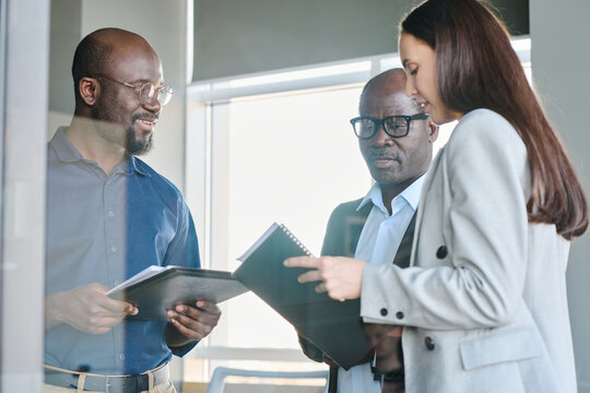 Group of confident intercultural brokers discussing financial documents or organizing new business event during working meeting in office