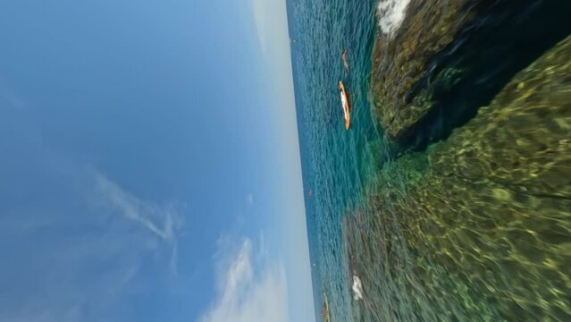 Cinematic vertical fpv shot above the sea passing by kayakers on orange kayaks