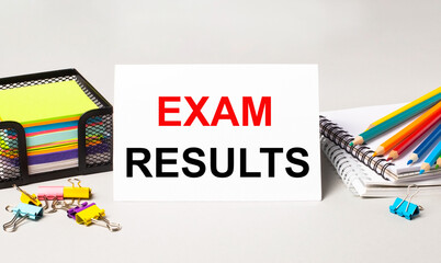 A paper card with the text EXAM RESULTS, multi-colored pencils, stickers and paper clips on the desktop.