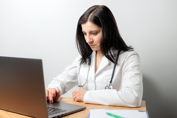 Female doctor, medic physician in white coat with stethoscope working on laptop at table