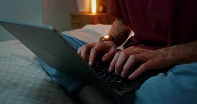A man is typing on a laptop, standing on his feet, sitting in a lotus position on the bed, Close-up of male hands on the keyboard, no face