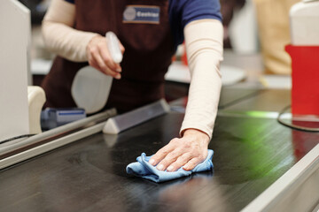 Close-up of cashier bending over checkout line in supermarket while spraying santizer on it and...