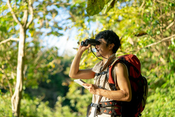 Asian young man with binoculars hiking in forest. Summer vacation.