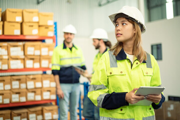 Professional female worker with teamwork wearing hard hat uses digital tablet computer for work. Goods and supplies on shelves with goods background in warehouse.logistic and business export