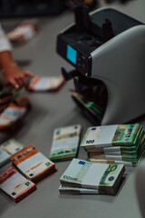 Fototapeta premium Bank employees using money counting machine while sorting and counting paper banknotes inside bank vault. Large amounts of money in the bank