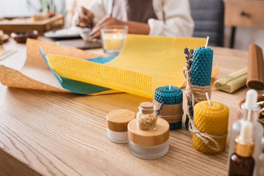 handmade candles near natural ingredients and wax sheets near cropped african american craftswoman on blurred background.