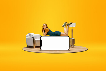 Positive smiling young girl lying on huge 3D model of mobile phone with empty screen for text, ad over yellow background with home interior. Online shopping, delivery. Mockup for ad, design, logo.