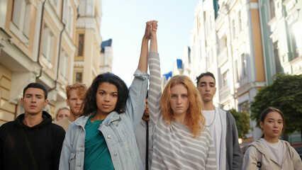 Two multiracial women holding hands together and lift them up in mass protest against racism