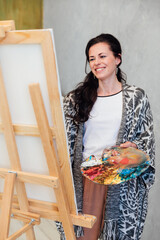 female artist with palette draws on easel in art studio