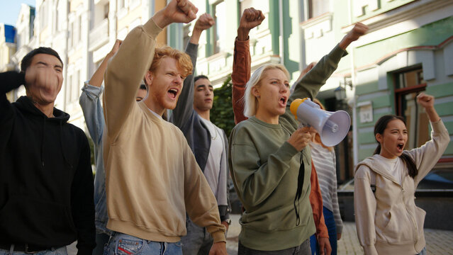 Woman leader at protest shouting slogans into megaphone. Multiethnic activist people at city streets