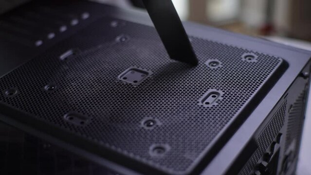 Close-up cropped shot of unrecognizable man cleaning dust off side of computer system case with fan using vacuum cleaner at desk. Concept of desktop PC maintenance and service. Shooting in slow motion