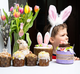 Cute little boy with bunny ears looking at tasty easter sweet cake
