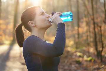 Sporty and athletic woman running and jogging drinking water from a bottle on a sunny winter morning in a forest
