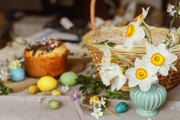 Beautiful daffodils on background of homemade easter bread, natural dyed easter eggs with spring flowers on linen napkin on rustic table. Traditional Easter food