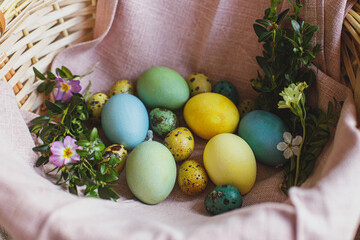 Happy Easter! Stylish natural dyed easter eggs with spring flowers on linen napkin in wicker basket. Traditional Easter food. Top view. Rustic Easter still life