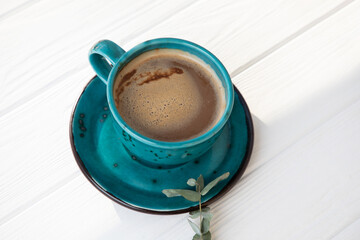 Blue mug with coffee, cappuccino on a white wooden background with eucalyptus branch. Top view, close-up