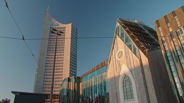 The outside of the university of Leipzig and a skyscraper in Saxony, Germany. The building is a transformed church and showcases modern architecture.  During sunrise golden hour.
