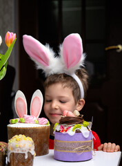 Cute little boy with bunny ears looking at tasty easter sweet cake