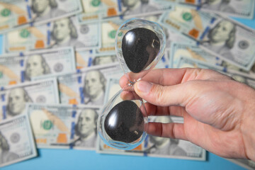 Male hand holding hourglass over dollars. Time is money