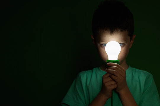 Little boy with light bulb in dark room
