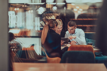 Photo through the glass of a group of business people sitting in a cafe and discussing business plans and ideas for new online commercial services