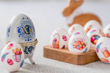 A large egg-box with the inscription XB, an Easter bunny and Easter eggs on a linen tablecloth on the table. The concept of the Bright Easter holiday.