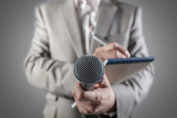 Journalist at a news press conference or media event holding a microphone and writing notes