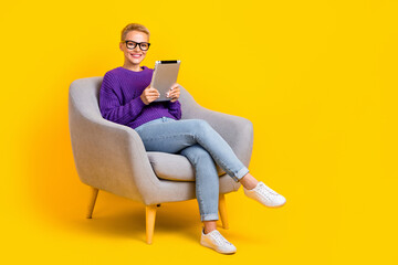 Fototapeta na wymiar Full size portrait of positive friendly person sit chair hold use tablet empty space isolated on yellow color background