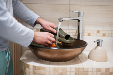 Сleaning the shoes. Man washes rubber slippers in the sink.