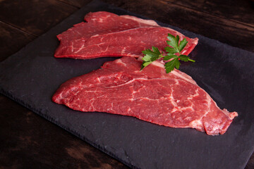 Raw minute steak of marbled beef with a parsley leaf on a stone slate board