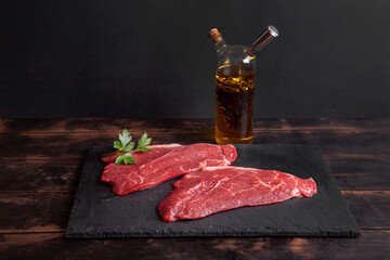 Raw minute steak of marbled beef on slate board, bottle with vegetable oil and balsamic vinegar