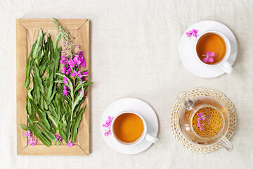 Herbal tea from kipreya leaves in white cups on linen fabric table background, fireweed green leaves and flowers on wooden tray. Flavored herbal tea from natural plants, healing hot beverage.