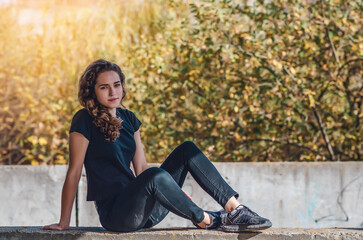Resting teenage girl sitting on the ground. Dreamy eyes. Sunset background.