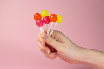 Female hand holding different lollipops on a pink background