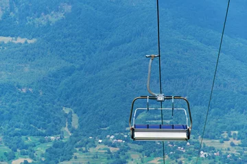 Poster Im Rahmen Gondeln Ski lift chair hanging on a cable against the backdrop of summer mountains  © Rejdan