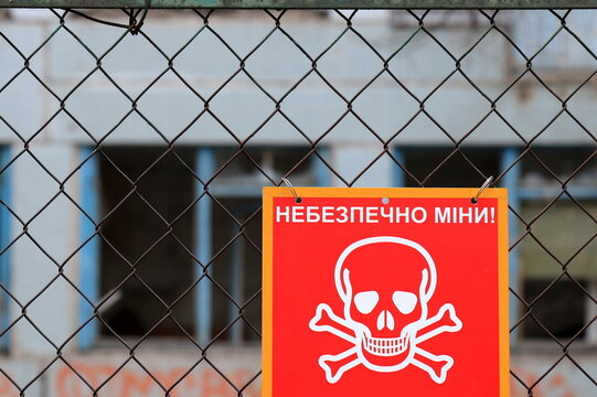 Danger mines - Red sign with inscription in Ukrainian, Skull and crossbones - sign of death from military mine against of destroyed building, Russia war against Ukraine,