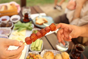 a person is holding a skewer of sausage on a stick with other people around it and a picnic table with food