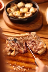 a person cutting up a piece of meat on a cutting board with a fork and knife in it and a bowl of potatoes and a bowl of other food in the background