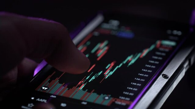 A man holds a smartphone in his hands, buys stocks, deals with crypto and trading. The male palm has a phone, controls the fingers on the screen in the investment management application. Neon light