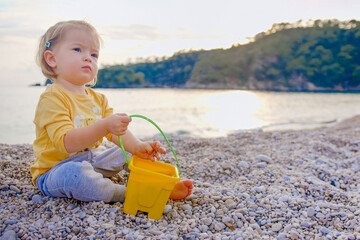 Rest on the sunset sea. A cute child throws pebbles and has fun. Little girl is playing on the...