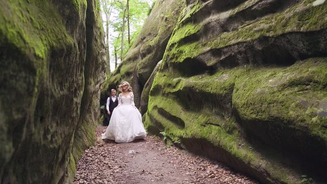 Cute bride and groom runs between the rocks with a great smile