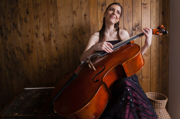 A creative cellist is playing the cello against a wooden background. © Georgi