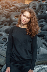 Fototapeta premium Dramatic photo of a sad girl at a tire repair dump. Waste disposal.