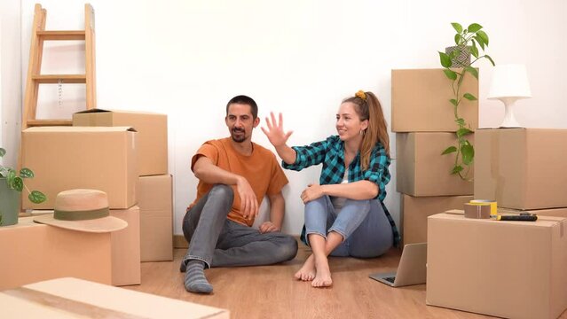 Happy couple moving home resting and talking in empty apartment with boxes making plans together and high five celebrating new life.